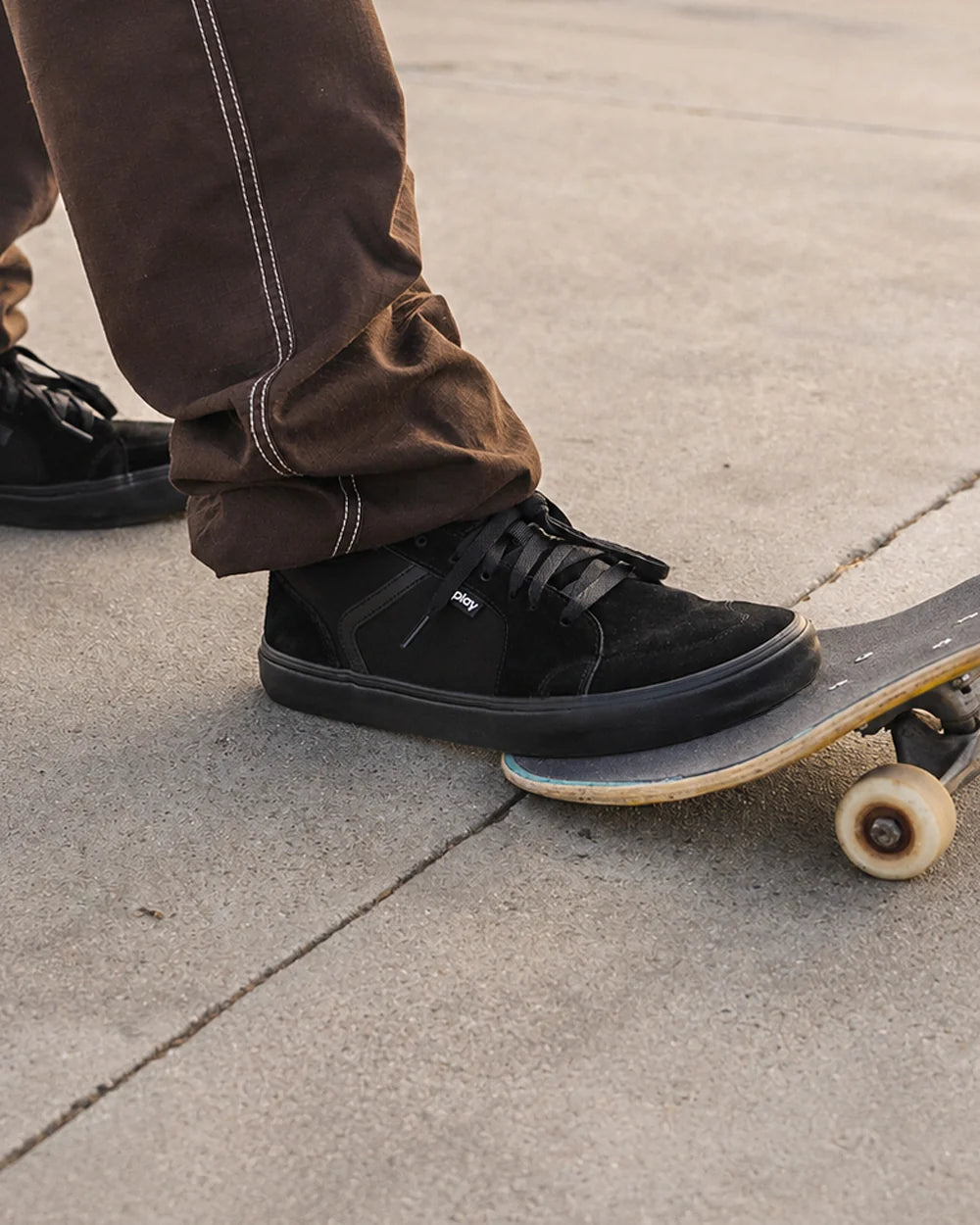 Person wearing low-profile black sneakers on a skateboard on a sidewalk.