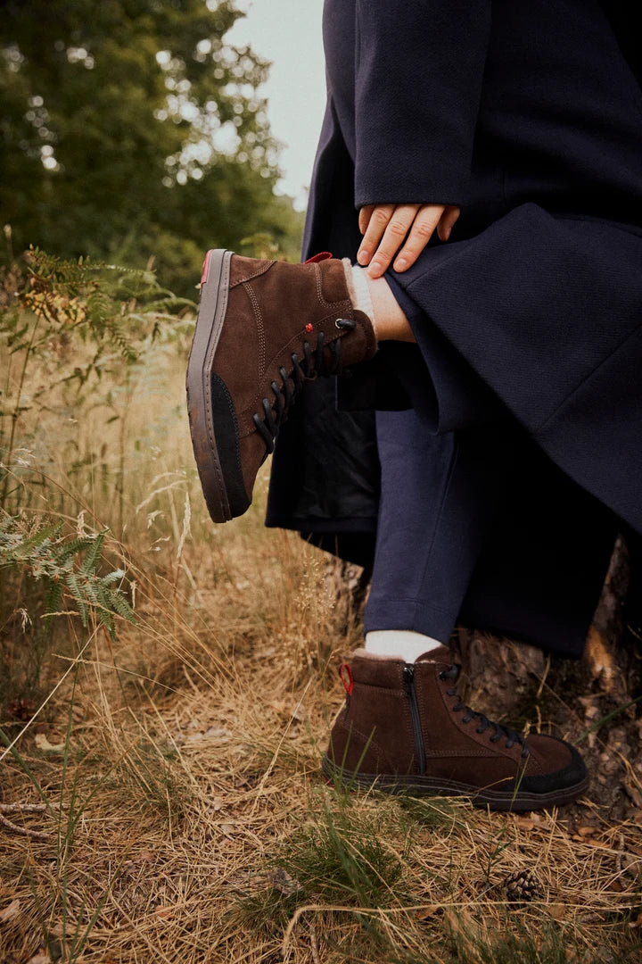 Person wearing brown lace-up ankle boots on a path through grass.