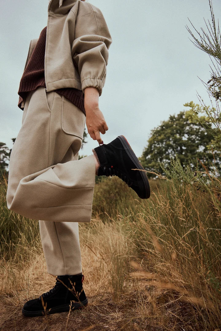 Person wearing black ankle boots on a grassy path, viewed from the side.