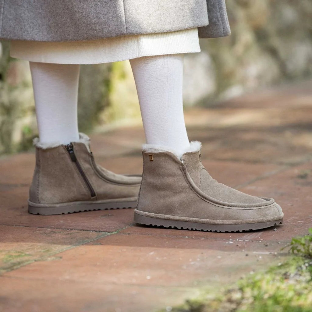 Botines beige con forro de lana, llevados con medias claras sobre un camino.
