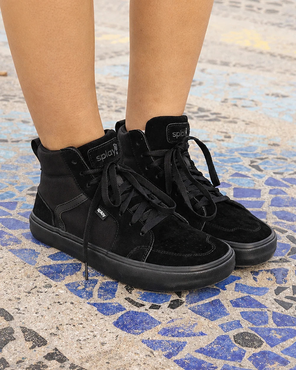 Persona con zapatillas negras de caña alta apoyadas sobre un suelo de mosaico.